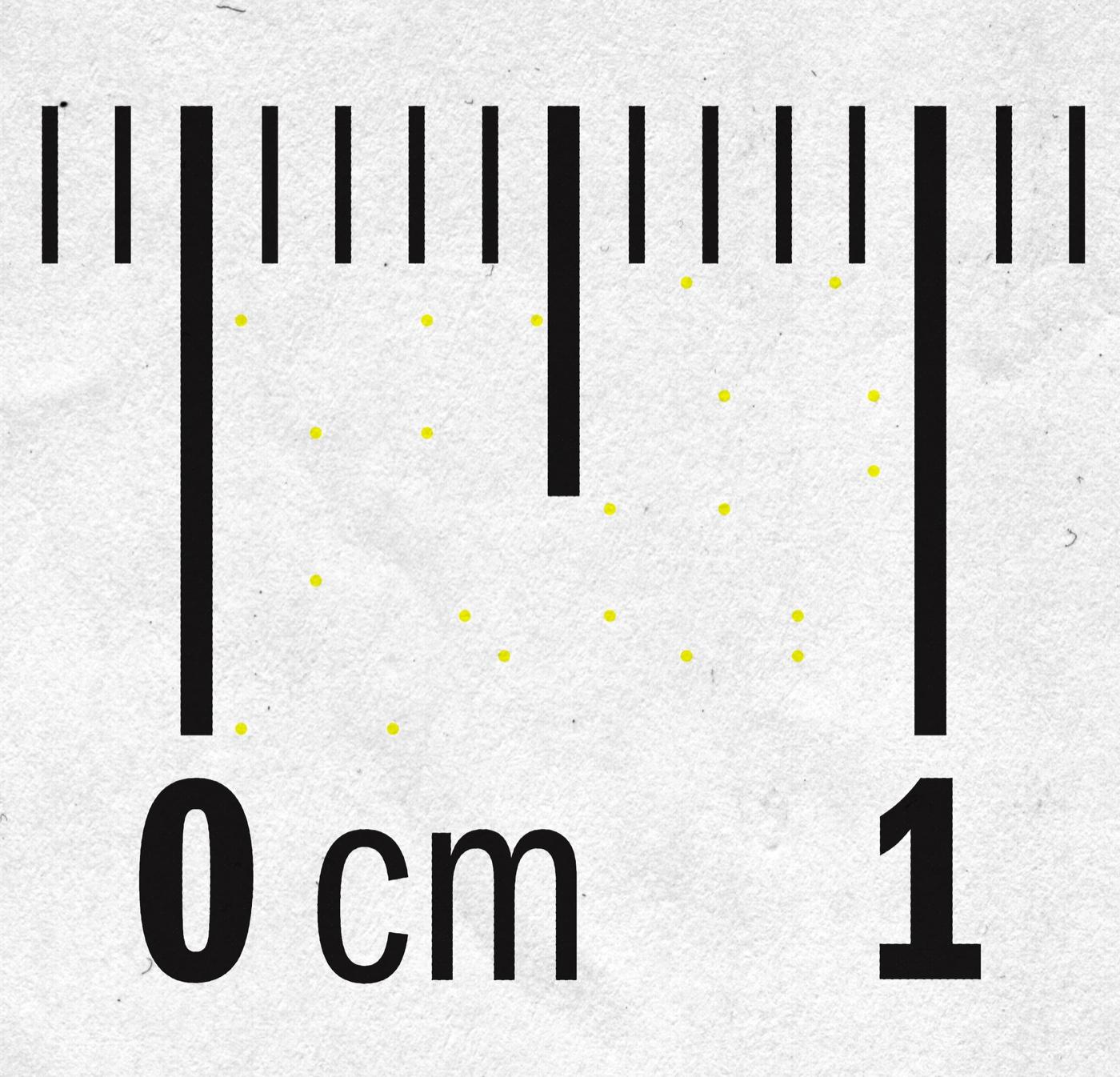 Enlarged view of a printed page showing a sparse grid of small yellow dots against paper, with a centimetre ruler along one edge for scale