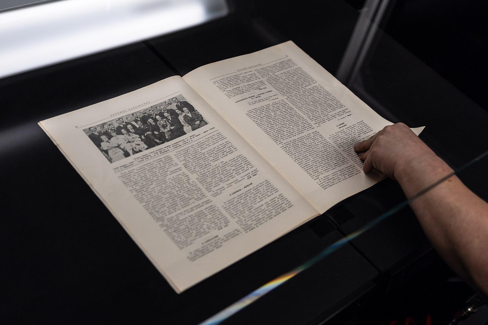 Operator digitising a bound volume on a manual overhead book scanner, the book open on a cradle beneath an overhead imaging head
