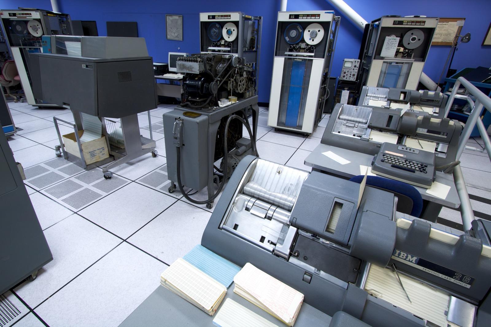 Restored IBM 1401 installation showing a line printer in the foreground with keypunch machines along one side and tape drives behind