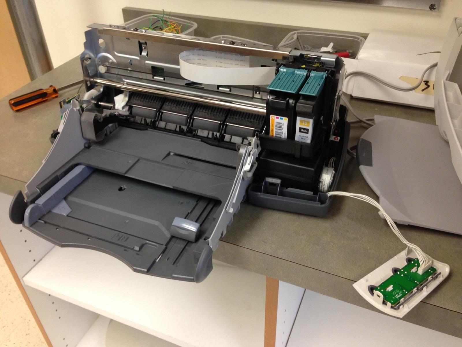 An inkjet printer with its covers removed, exposing the carriage rail, print head, and paper-feed rollers