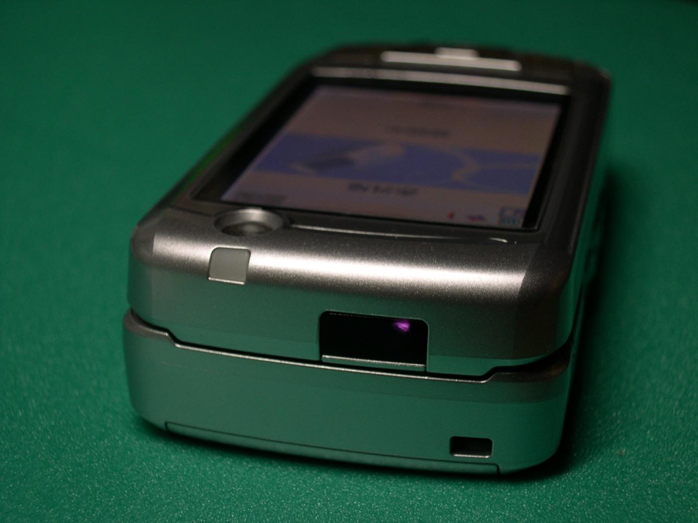 Top edge of a 2005 NTT DoCoMo clamshell phone, its infrared window emitting a faint violet glow captured by a digital camera